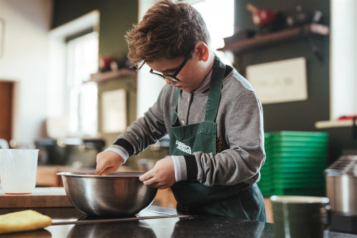 Child in glasses mixing ingredients in a metal bowl on a kitchen counter.