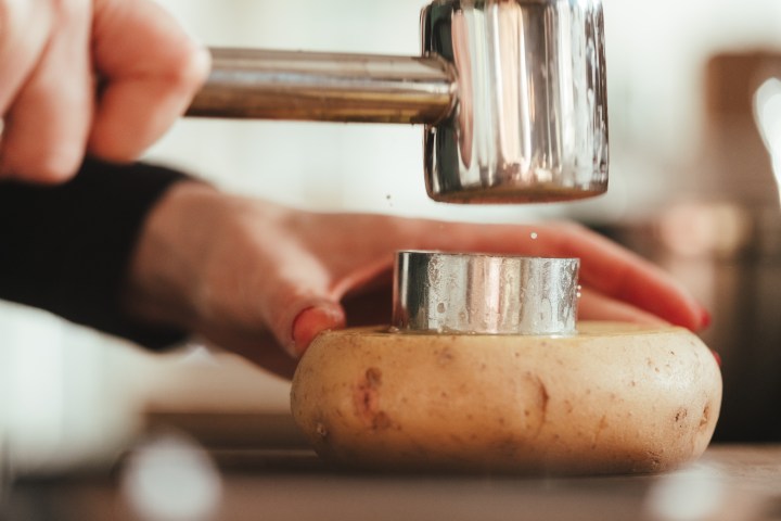 Close-up of a person using a mallet to press a metal cutter into a potato.