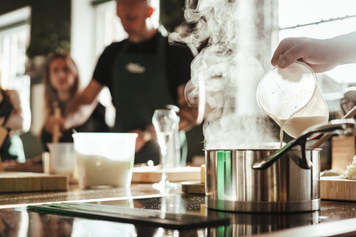 Person pours liquid into a steaming pot in a kitchen setting.
