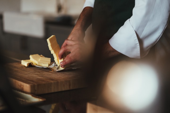 A person in a chef's uniform handling butter blocks on a wooden cutting board.