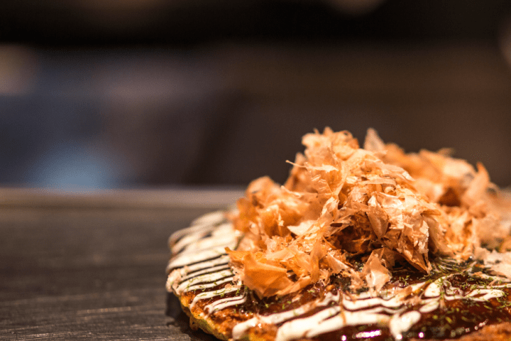 Okonomiyaki pancake topped with bonito flakes on a griddle.