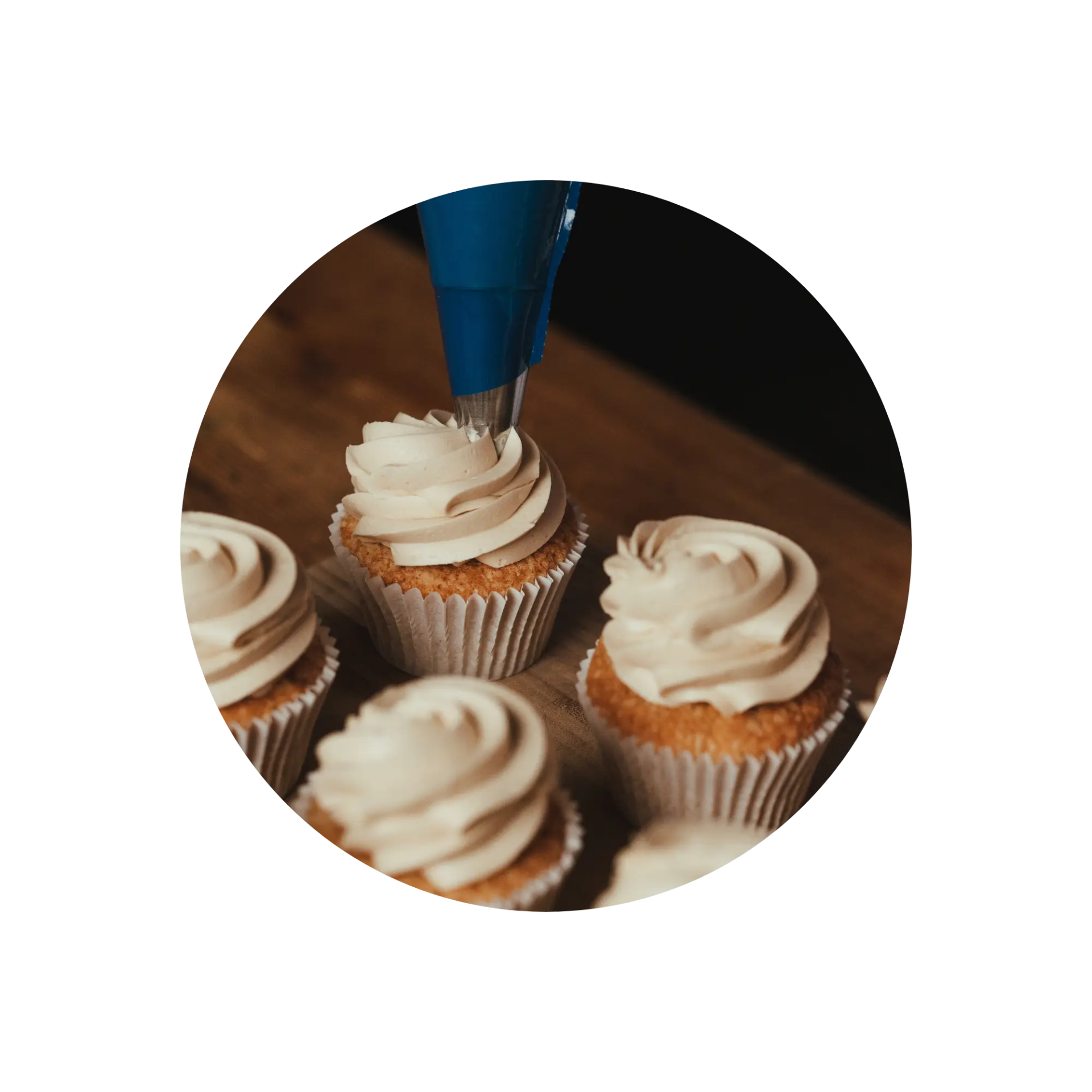 Cupcakes being frosted with a blue piping bag on a wooden surface.