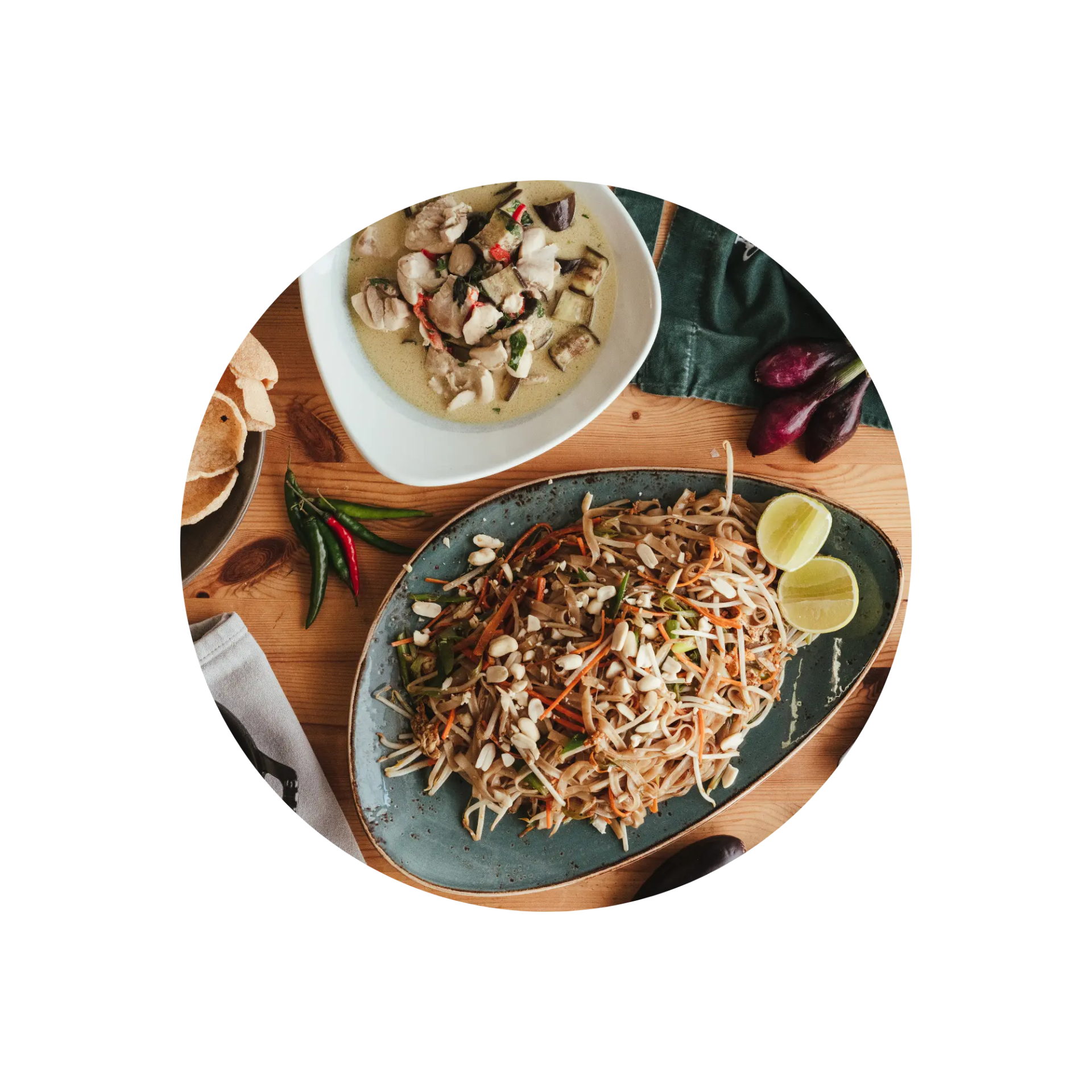 Top view of Thai green curry and pad thai with lime on a wooden table.