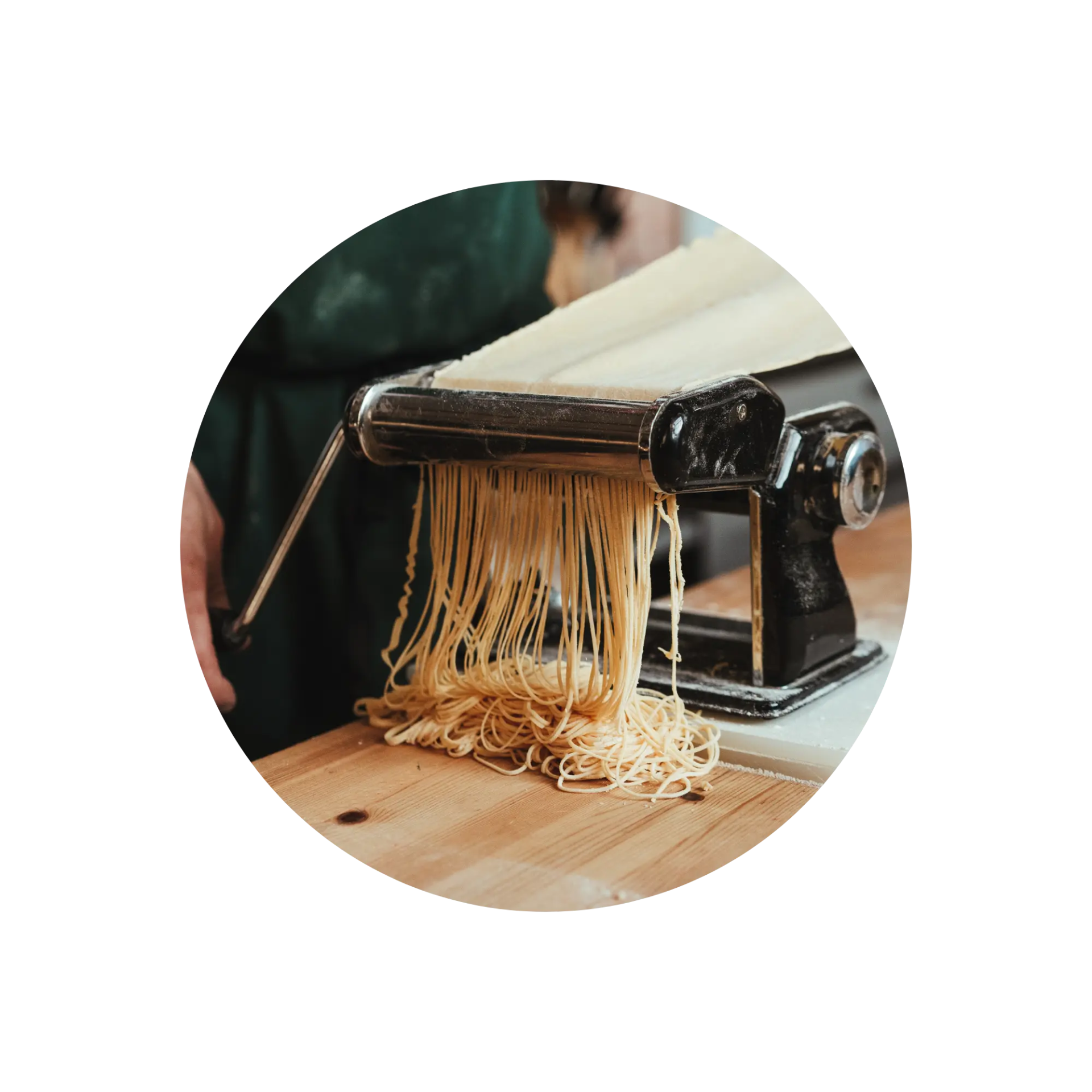 Homemade pasta emerging from a manual pasta machine on a wooden surface.