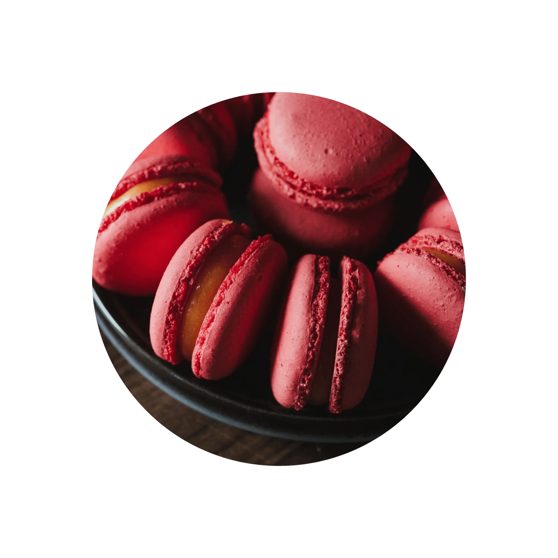 Close-up of red macarons with yellow filling on a black plate.