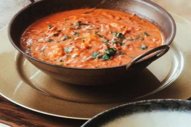 A bowl of tomato-based curry garnished with herbs on a plate.